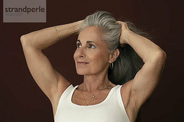 Thoughtful woman with hands in hair against maroon background