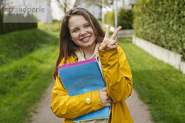 Smiling girl showing peace sign and holding colorful folders