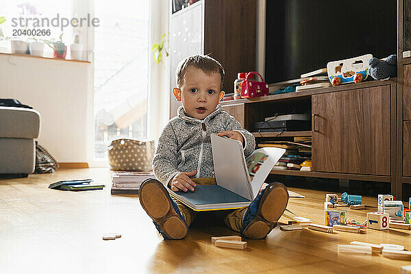 Cute boy with picture book sitting on floor at home