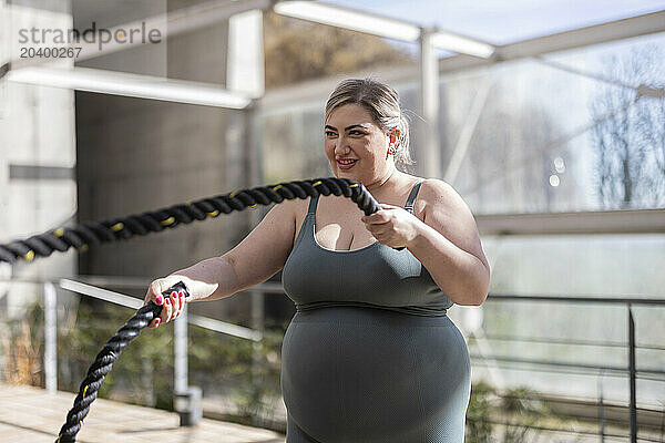 Smiling curvy young woman exercising with rope at park