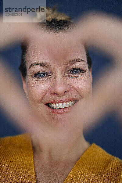 Happy beautiful woman showing heart shape with fingers against colored background