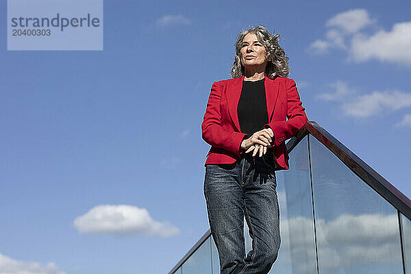 Confident businesswoman leaning on railing under sky