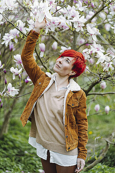 Beautiful redhead woman looking at magnolia blossom in park