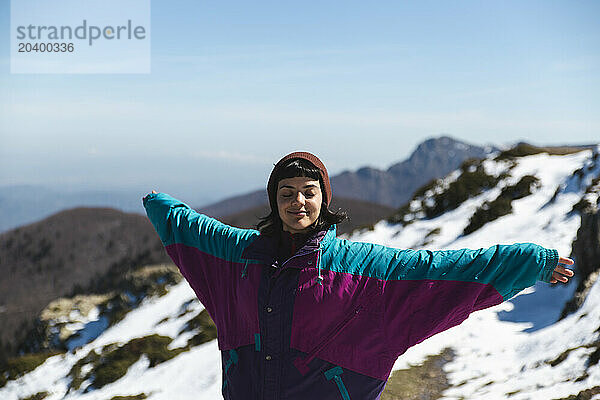 Carefree woman in winter coat standing with arms outstretched on mountain