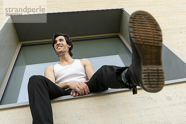 Smiling young man sitting carefree on window