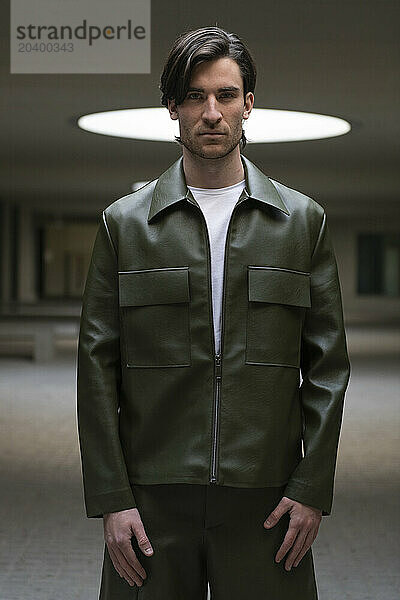 Fashionable young man wearing green leather jacket in illuminated parking garage