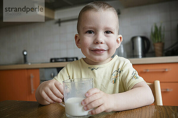 Cute boy drinking milk sitting in kitchen at home