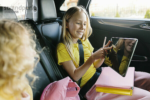 Girl sharing tablet PC with sister sitting in car