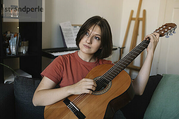 Beautiful young woman practicing acoustic guitar on sofa at home