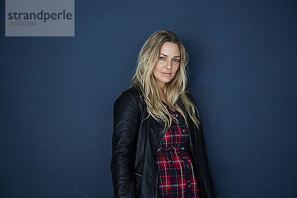 Confident blond mature woman wearing jacket against colored background