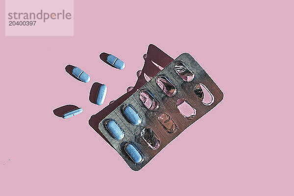 Blue pills and blister pack over pink background