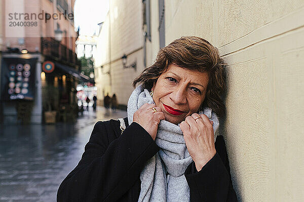 Smiling woman wearing scarf and leaning on wall