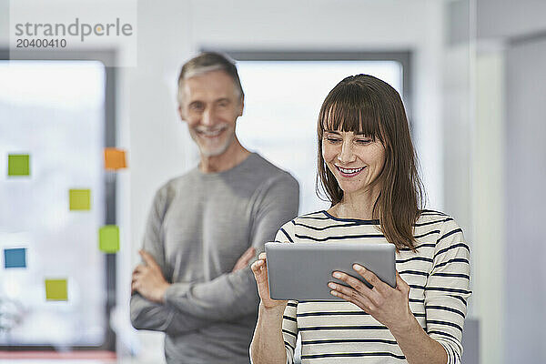 Smiling businesswoman using tablet PC with colleague in background