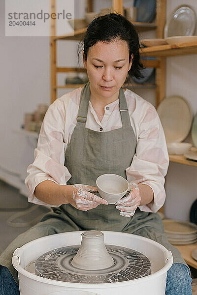 Confident craftsperson with clay bowl over pottery wheel at art studio