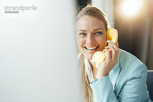 Happy businesswoman talking through telephone receiver in office