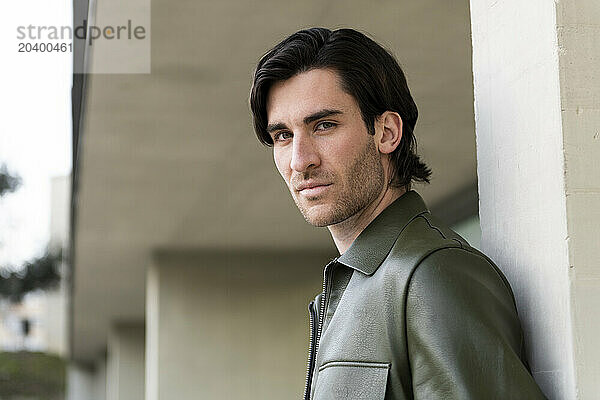 Fashionable young man wearing leather jacket leaning on column