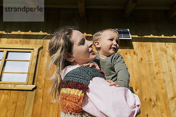 Mother carrying son near house on sunny day