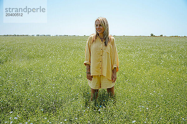 Smiling woman wearing yellow linen clothing standing in blooming field on sunny day