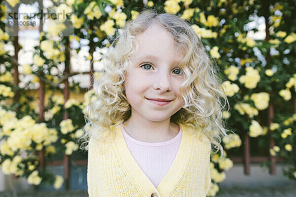 Smiling blond curly haired girl standing in front of yellow flowers