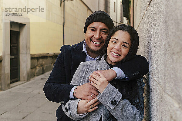 Happy couple standing near wall in front of building