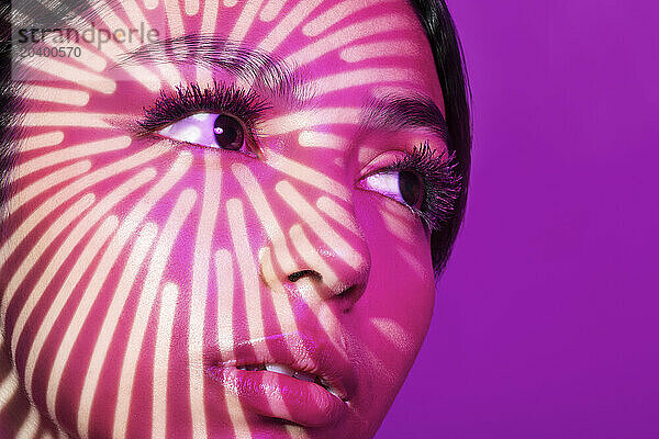 Young woman with light pattern on face against pink background