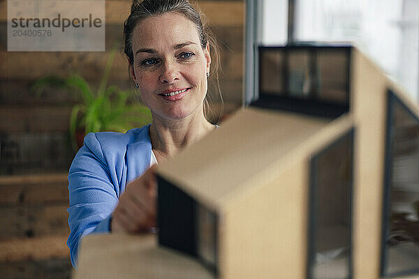 Smiling mature architect examining model house in office