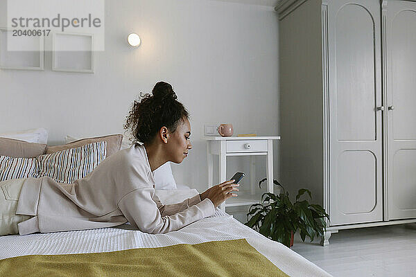 Young woman lying on bed scrolling on phone at home