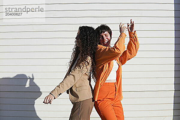 Happy lesbian couple dancing together in front of white wall