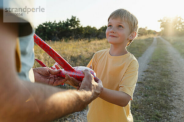 Smiling blond boy holding toy airplane with father at meadow