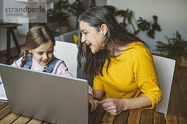 Happy grandmother and granddaughter using laptop at table at home