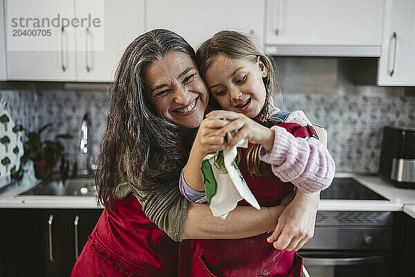 Happy grandmother embracing granddaughter in kitchen at home