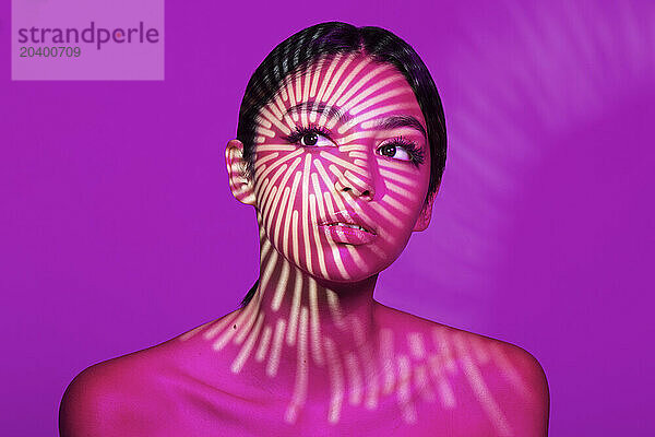 Beautiful young woman with light pattern on face against pink background