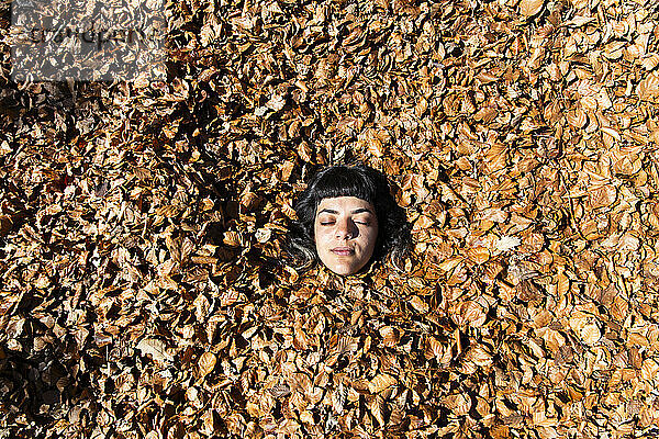 Young woman with eyes closed amidst fallen autumn leaves