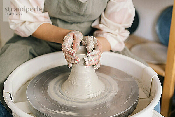 Craftsperson molding clay on pottery wheel at art studio