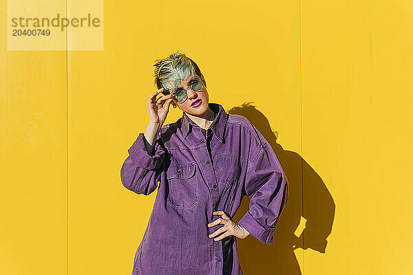 Woman wearing purple jacket posing in front of yellow wall