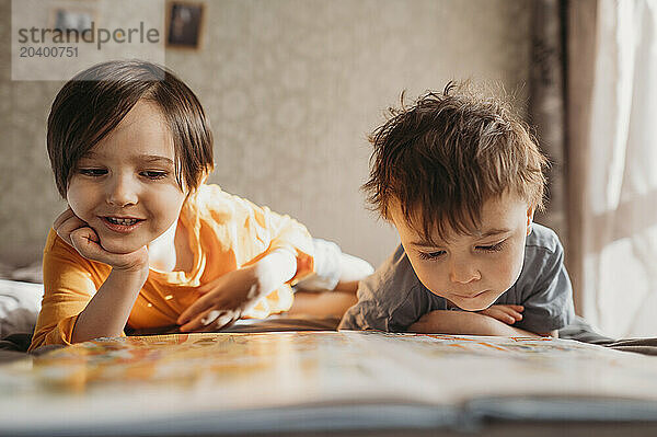 Cute siblings reading book together on bed at home