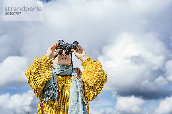 Smiling girl looking through binoculars under cloudy sky