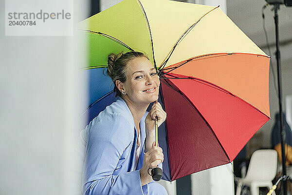 Happy businesswoman with colorful umbrella in office