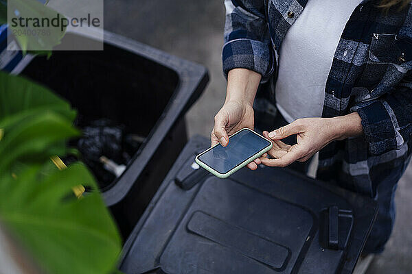 Mature woman using mobile phone near garbage bin