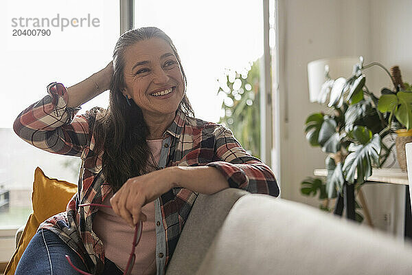 Smiling mature woman with eyeglasses sitting on sofa in living room at home