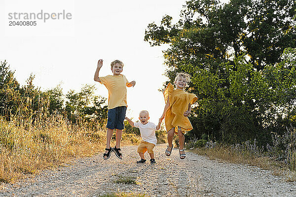 Happy siblings jumping on footpath at sunset