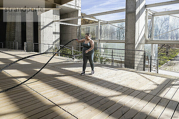 Curvy young woman exercising with rope on footbridge at park