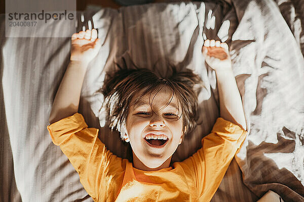 Cute playful boy with long hair lying on bed home