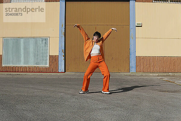 Confident woman dancing with arms raised in front of building on sunny day