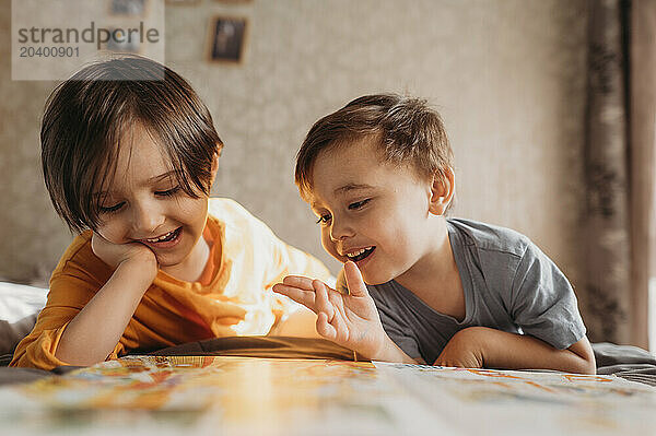 Happy cute siblings reading book together on bed at home