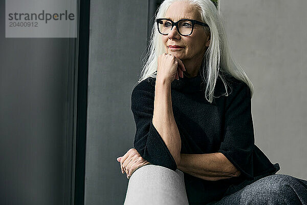 Senior woman sitting with hand on chin at home