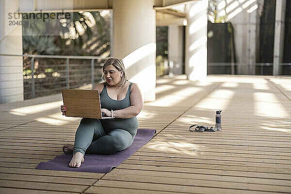 Curvy woman using laptop on footbridge in park