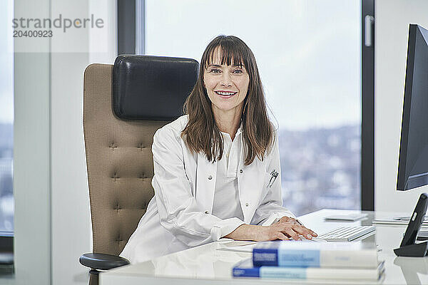 Portrait of smiling female doctor sitting at desk in medical practice