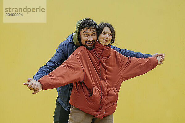 Happy couple with arms outstretched standing against yellow background