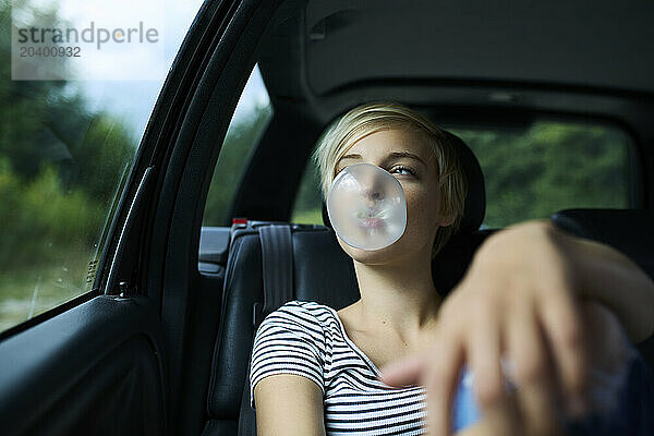 Young woman with eyes closed blowing bubble gum sitting in car